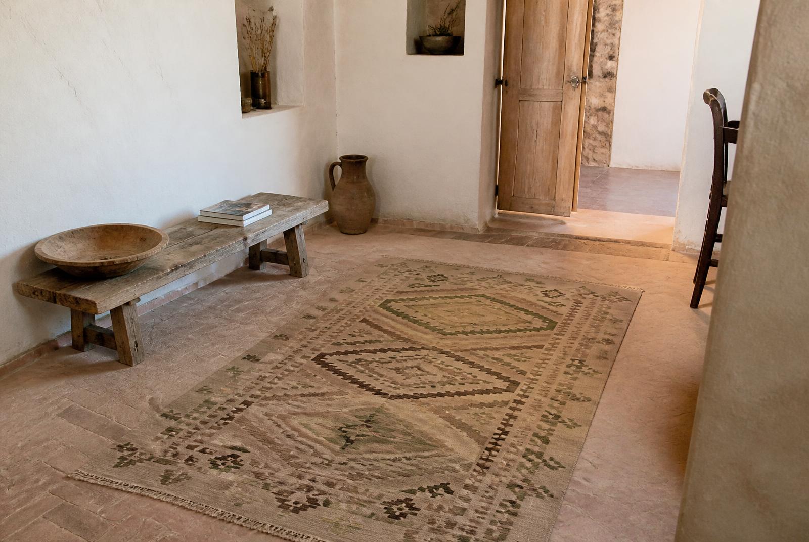 A flatwoven kilim on the terracotta floor of a Mediterranean stone house