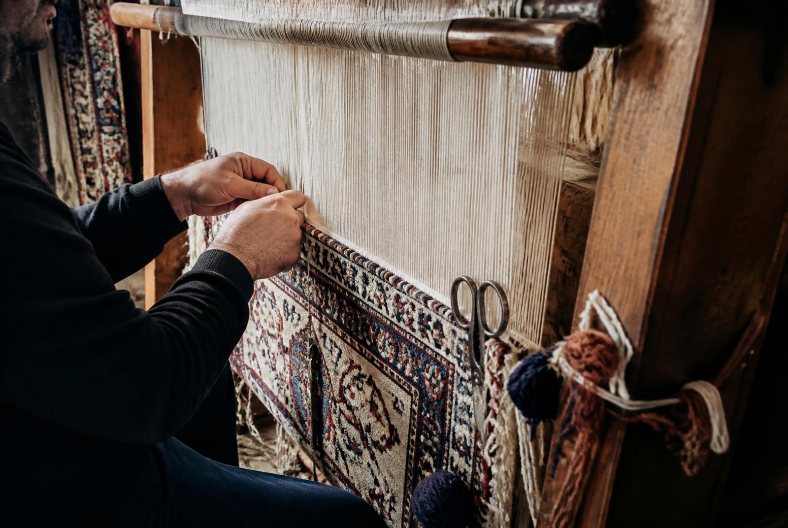 A weaver's hands tying knots at a traditional loom